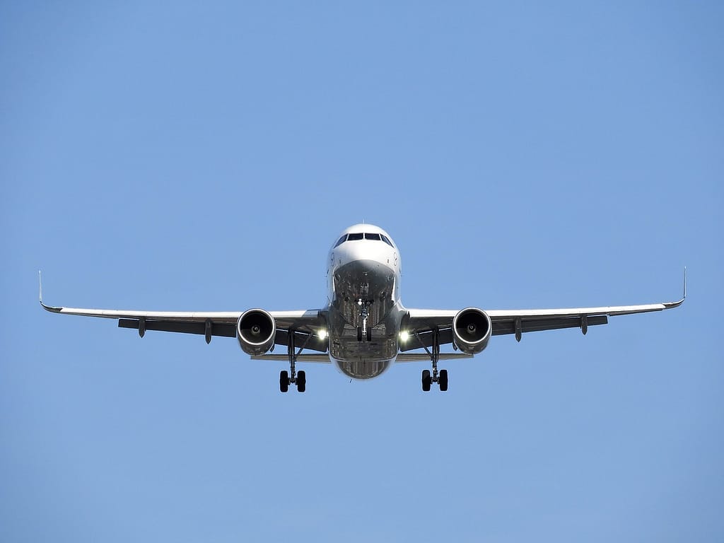 Aviao de grande porte se aproxima para pouso com trem de pouso aberto e luzes acesas. Ao fundo, o céu azul